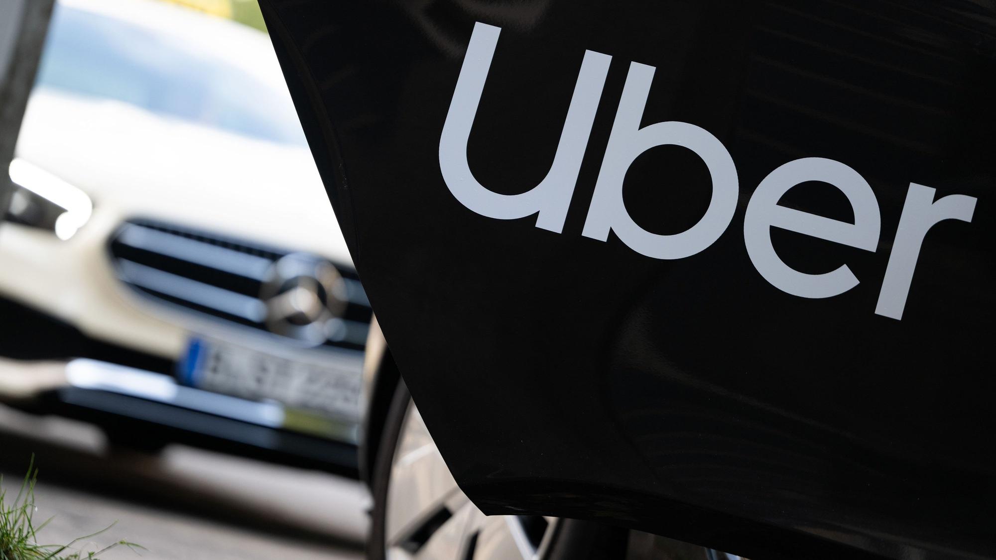 Ein Mietwagen mit einem Schriftzug des Fahrtenvermittlers Uber steht vor einem Taxi.