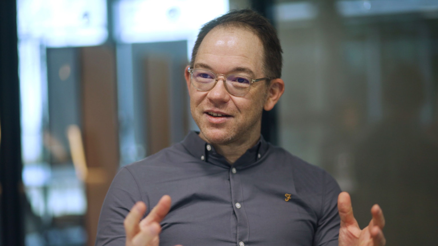 Ein Mann mit Brille und grauem Hemd in einer Gesprächssituation