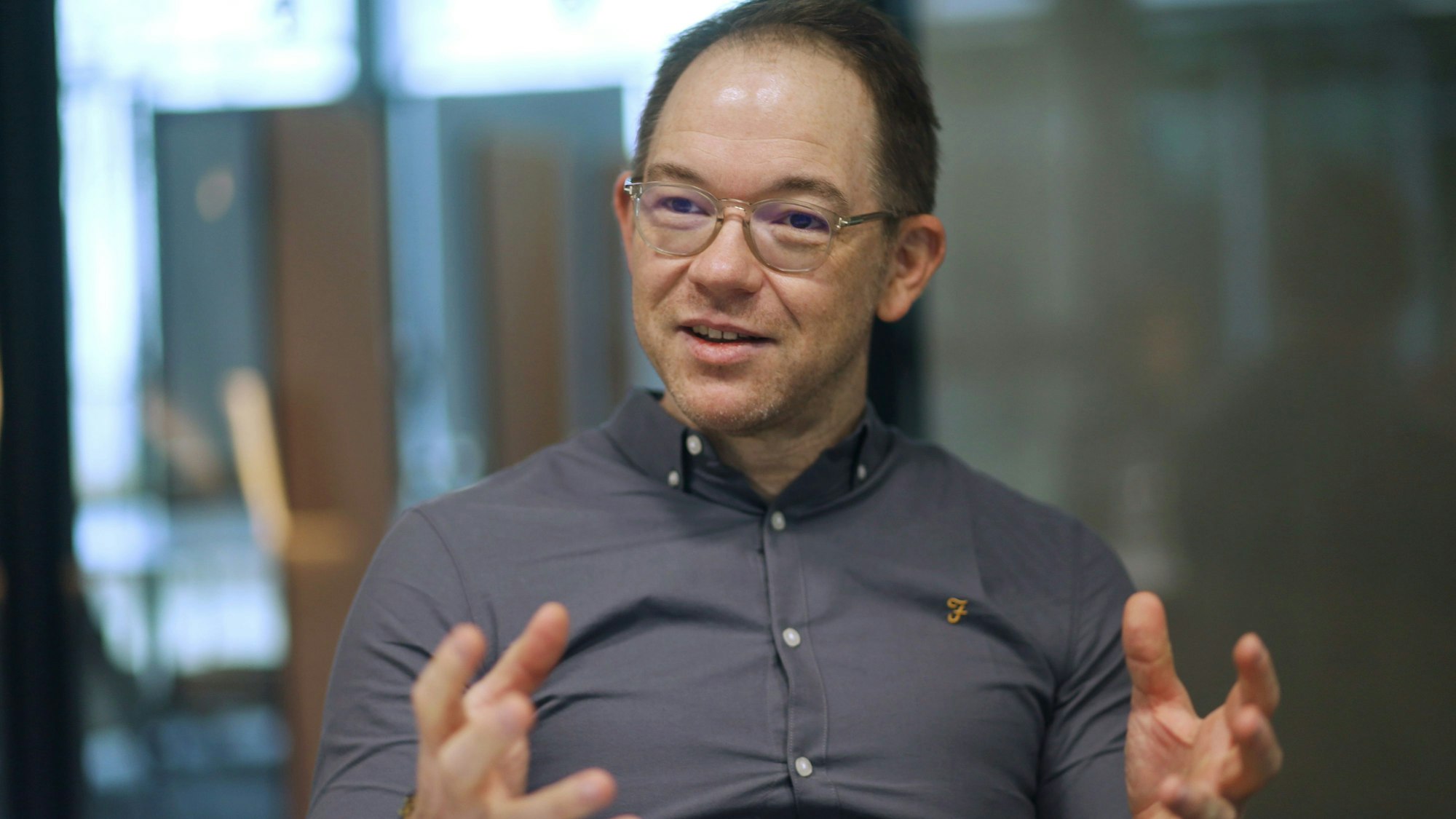 Ein Mann mit Brille und grauem Hemd in einer Gesprächssituation