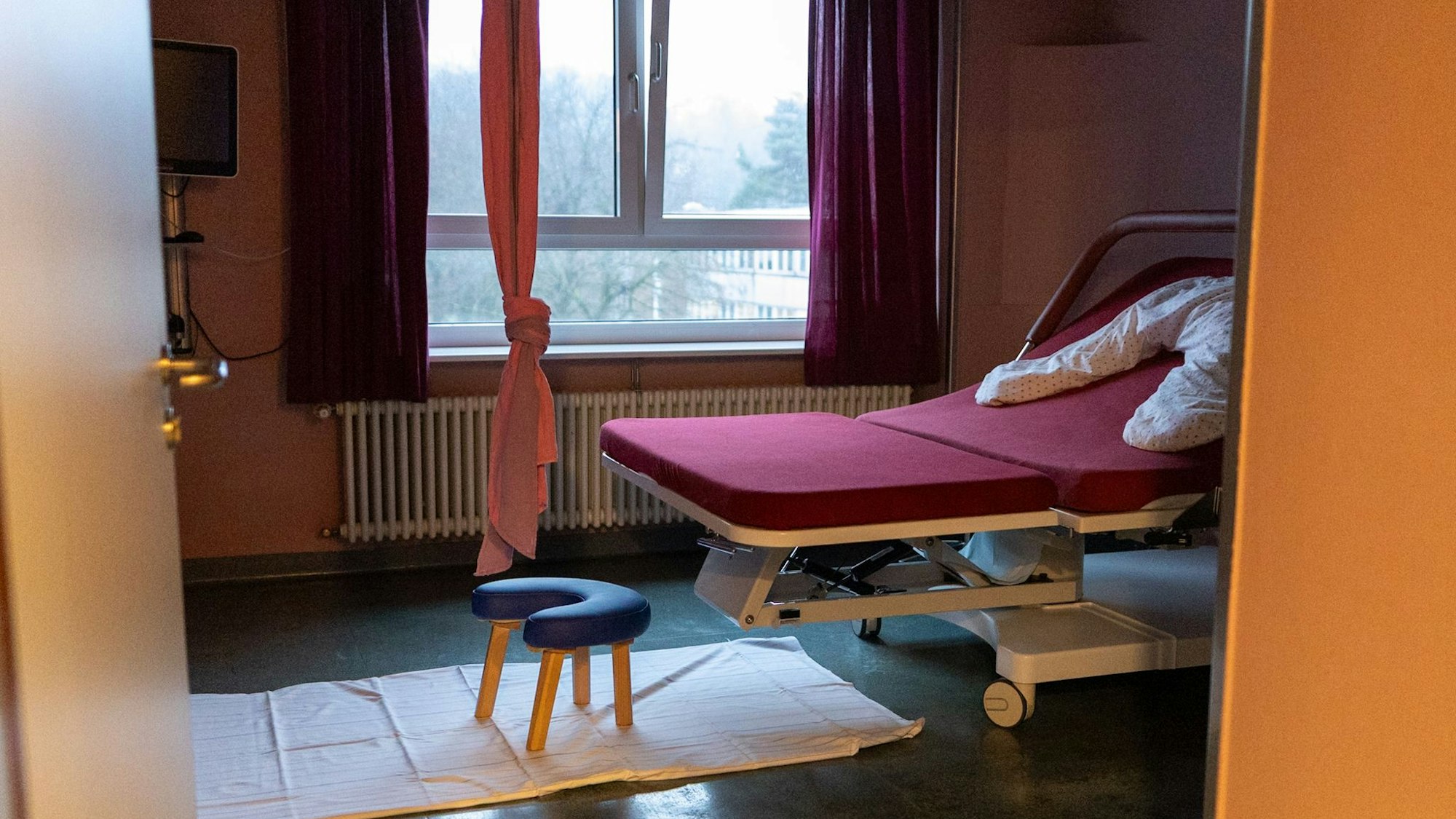 Blick in ein Bett im Kreißsaal. Ein Hocker steht davor. Ein Seil hängt von der Decke.