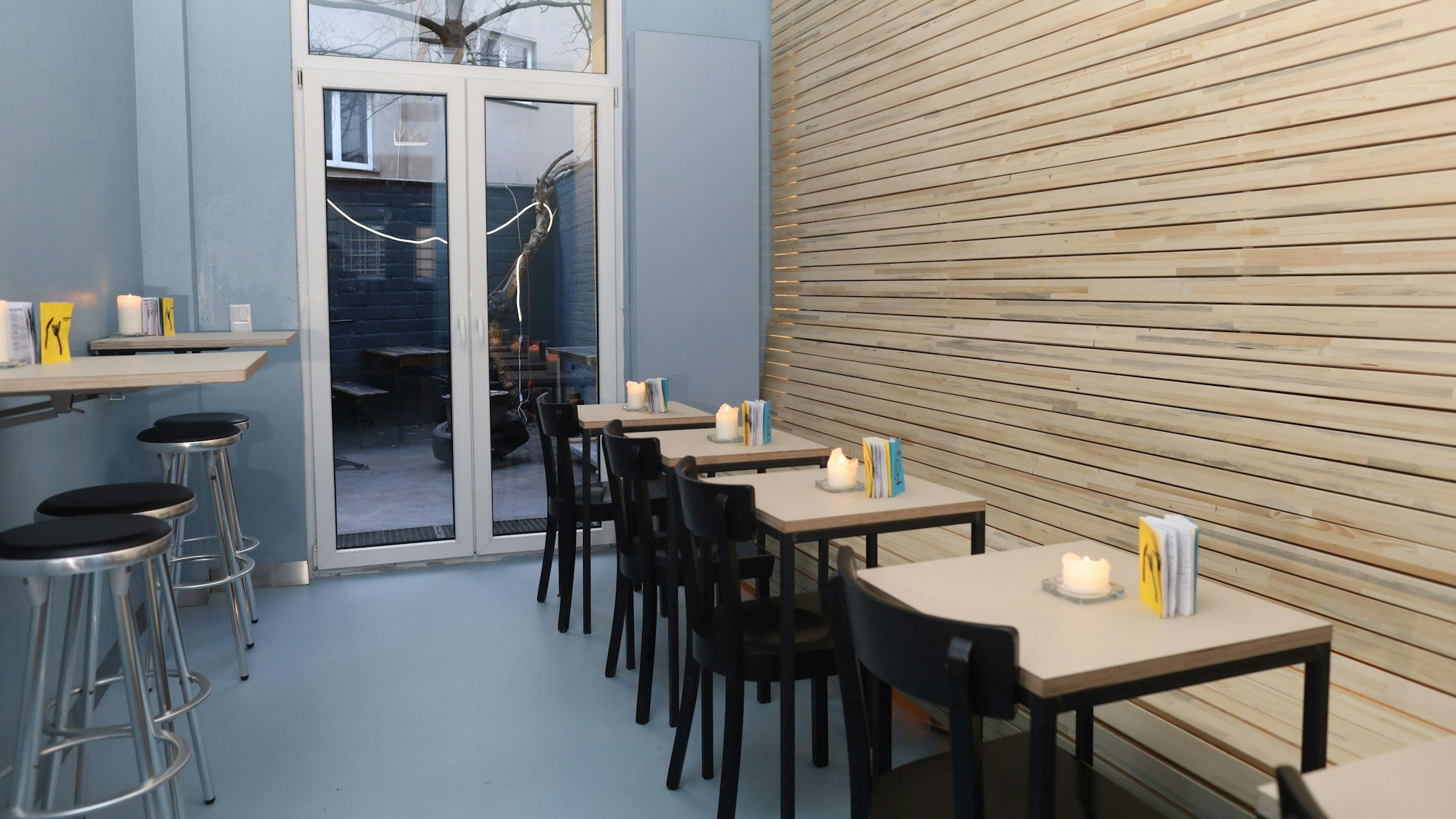 Der minimalistische gestaltete Gastraum mit grauen Wänden und einer holzvertäfelten Wand ist zu sehen.