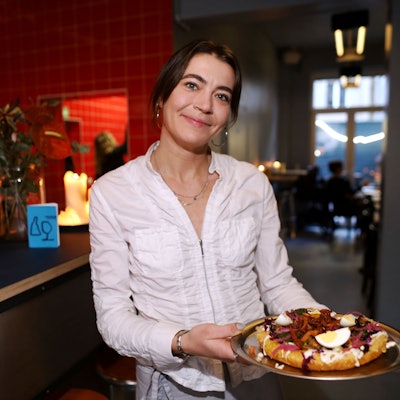 Eine junge Kellnerin zeigt das Gericht: ein Teigfladen mit Belag, unter anderem Ei.