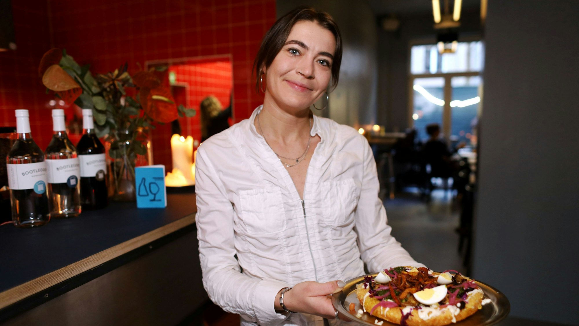 Eine junge Kellnerin zeigt das Gericht: ein Teigfladen mit Belag, unter anderem Ei.