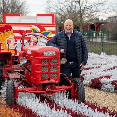 Peter Zens ist der Inhaber des Gertrudenhof. Er steht an einen alten Schau-Traktor gelehnt im Blumenbeet.