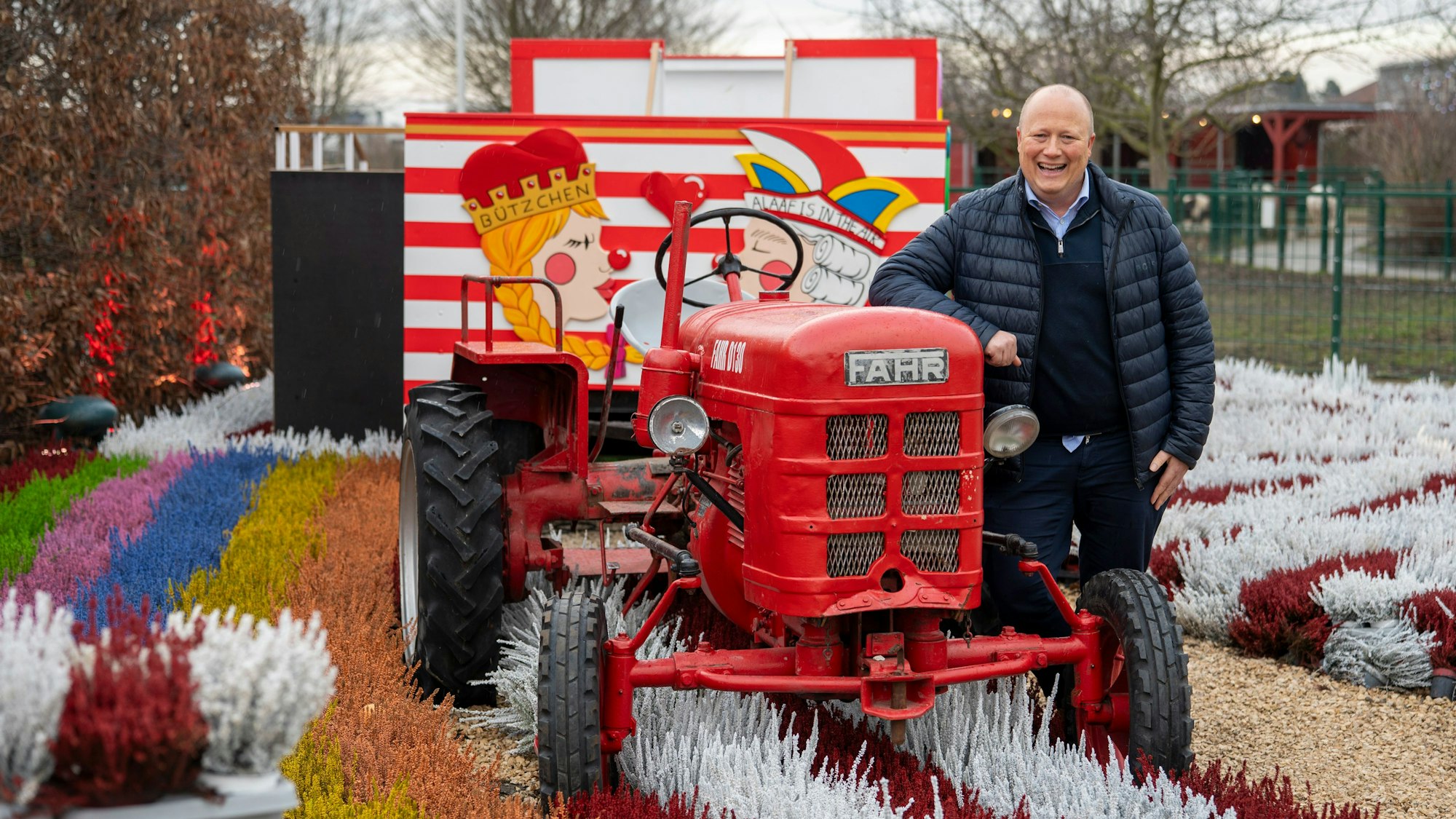 Peter Zens ist der Inhaber des Gertrudenhof. Er steht an einen alten Schau-Traktor gelehnt im Blumenbeet.