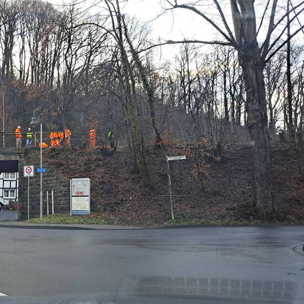 Menschen in orangefarbener Warnkleidung stehen auf der zu erneuernden Bahnbrücke über die Lüghauser Straße in Rösrath-Hoffnungsthal.
