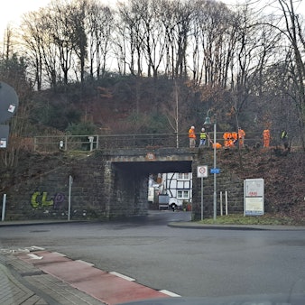 Menschen in orangefarbener Warnkleidung stehen auf der zu erneuernden Bahnbrücke über die Lüghauser Straße in Rösrath-Hoffnungsthal.
