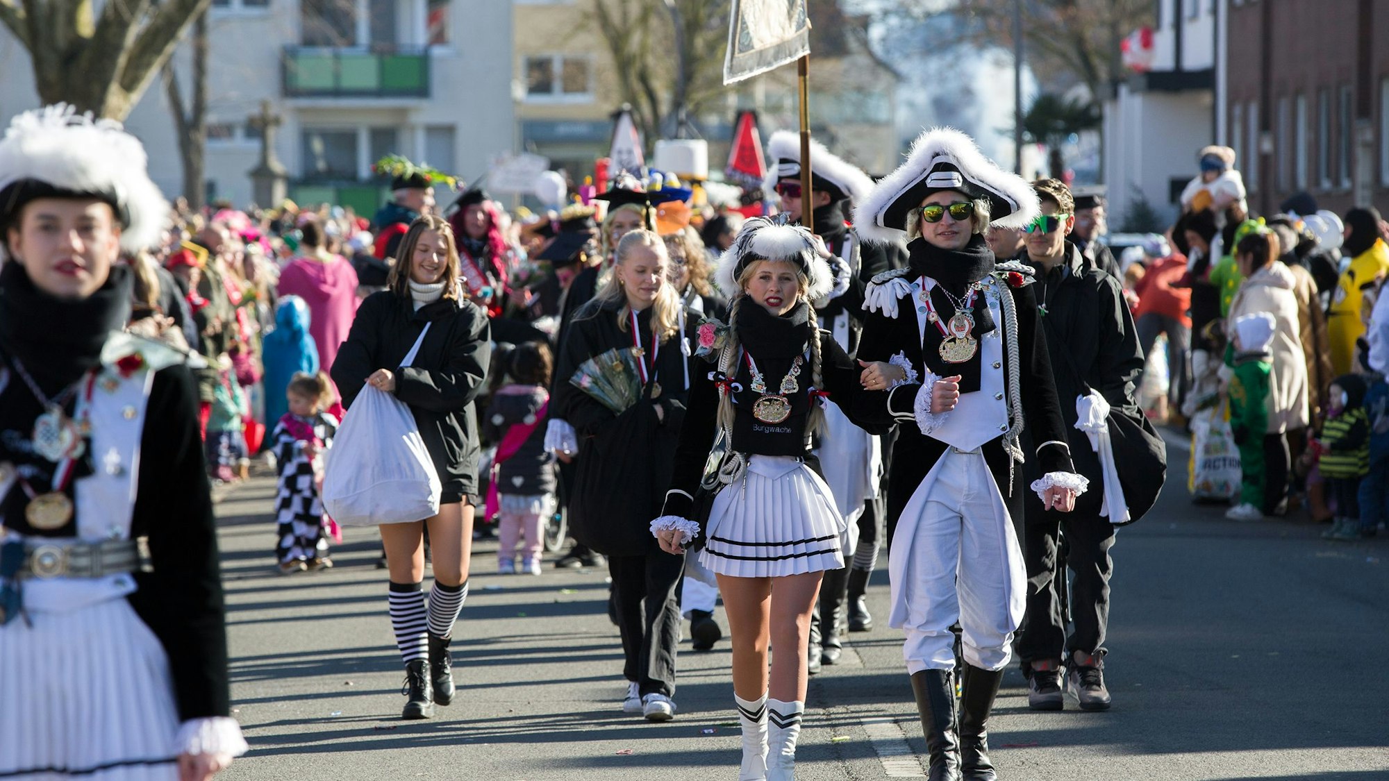 Eine Gruppe Karnevalisten in schwarz-weißer Uniform geht bei Sonnenschein im Karnevalszug mit.