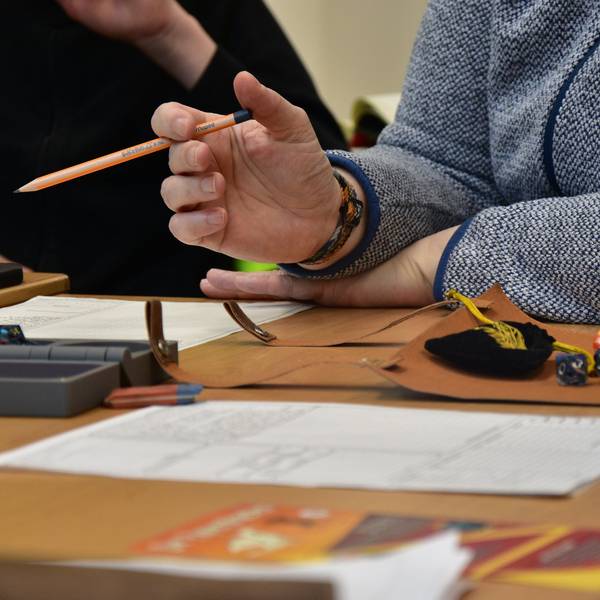 Block, Würfel und eine Person mit Bleistift an einem Tisch.