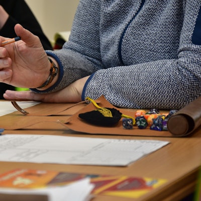 Block, Würfel und eine Person mit Bleistift an einem Tisch.