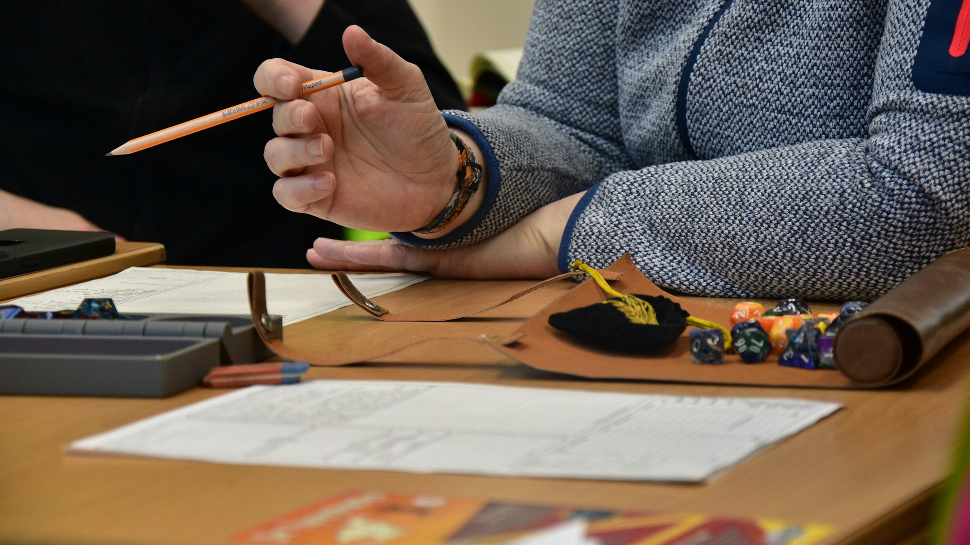 Block, Würfel und eine Person mit Bleistift an einem Tisch.