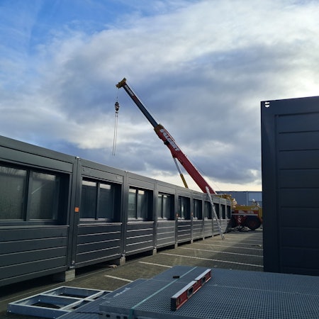 Die Aufnahme zeigt Container neben denen ein Kranwagen steht.