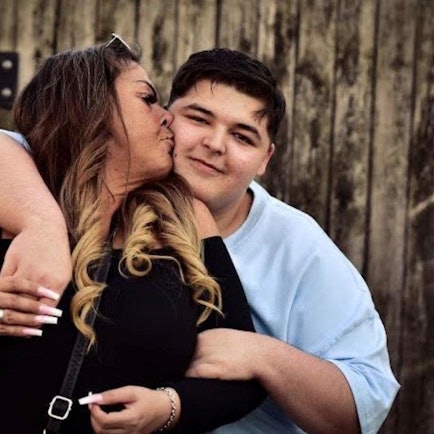 Auf dem Bild ist eine Mutter mit ihrem Sohn in inniger Umarmung zu sehen.