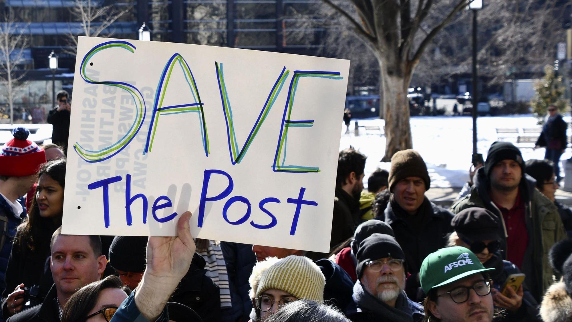 Eine Person hält bei einer Kundgebung ein Schild mit der Aufschrift „Save the Post“ hoch.