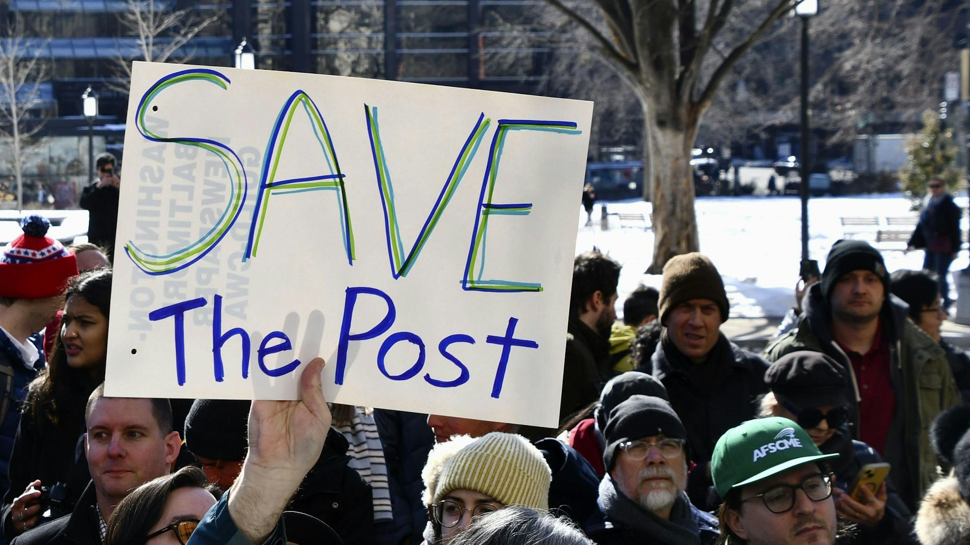 Eine Person hält bei einer Kundgebung ein Schild mit der Aufschrift „Save the Post“ hoch.