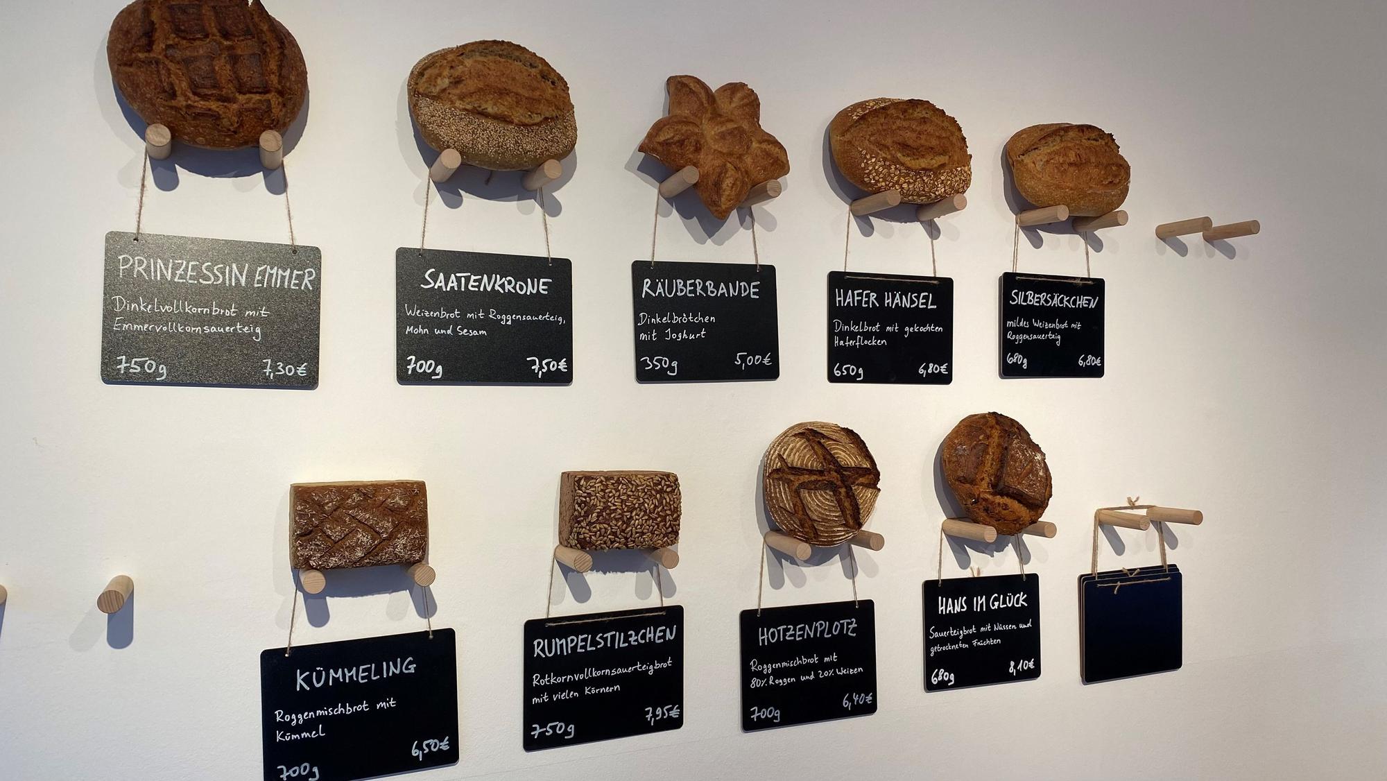 Zu sehen sind Brot-Laibe, die mit einer Beschriftung auf Wandhalterungen liegen.