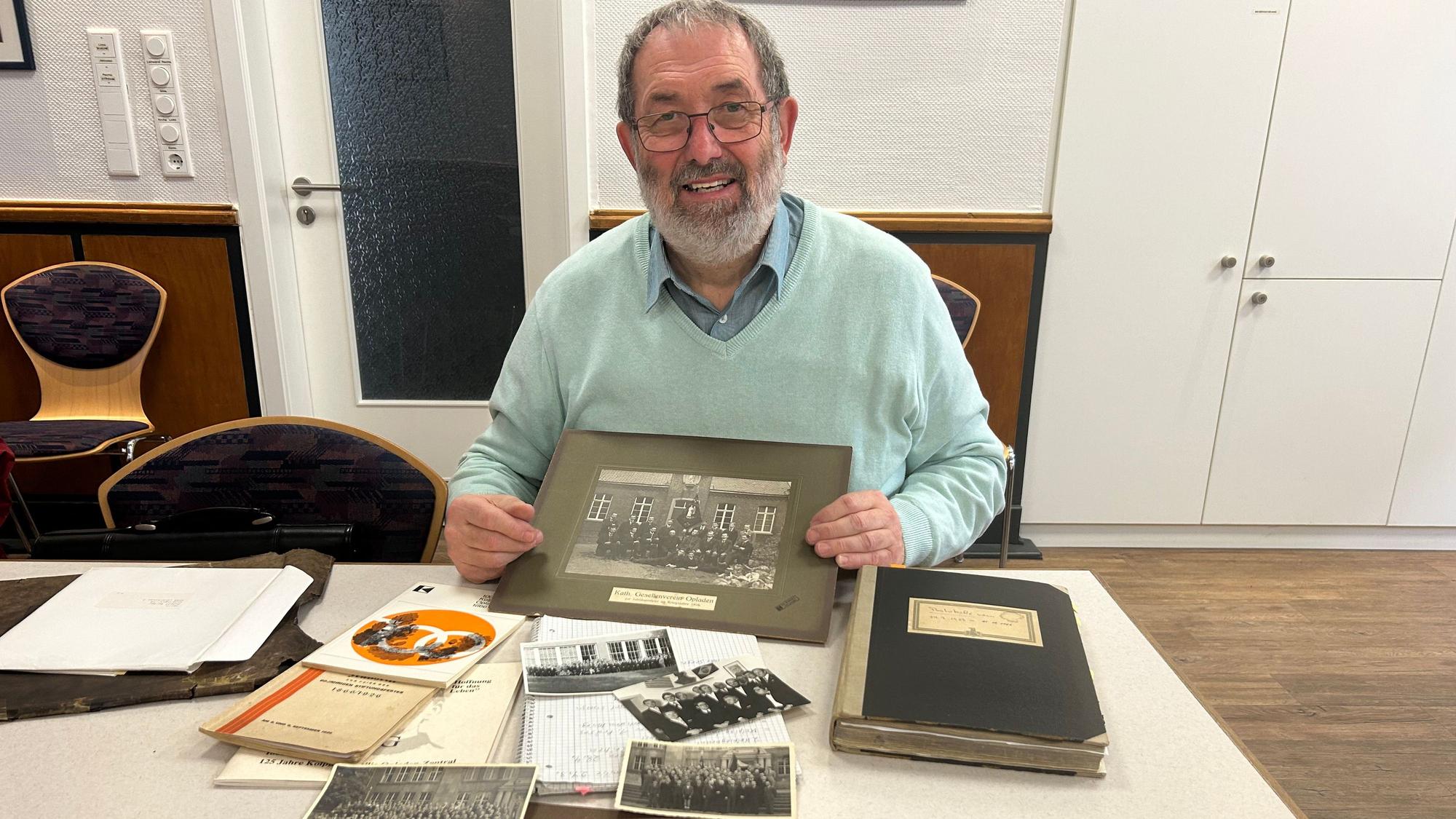 Ein Archivar sitzt mit alten Fotos an einem Schreibtisch.