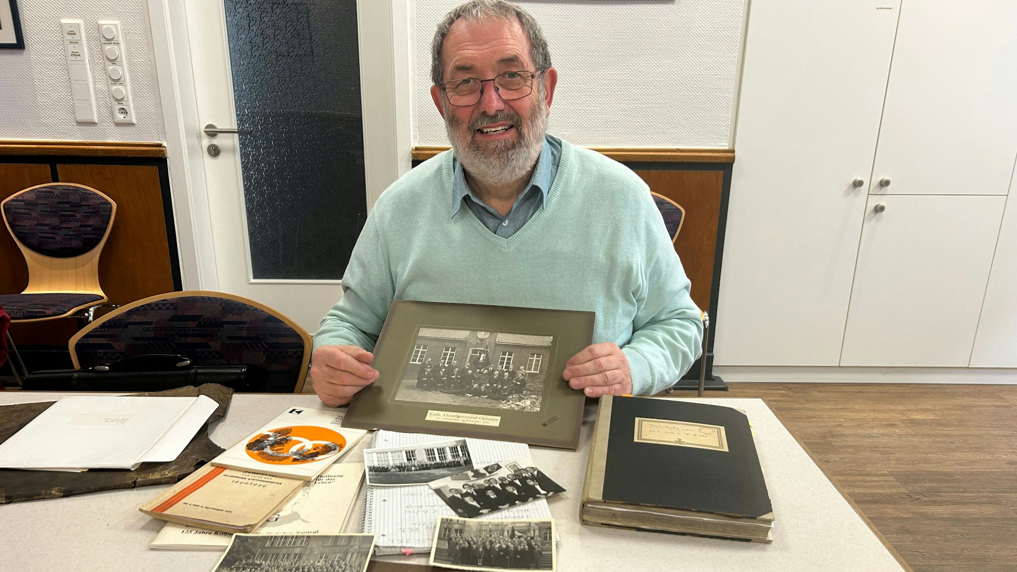 Ein Archivar sitzt mit alten Fotos an einem Schreibtisch.