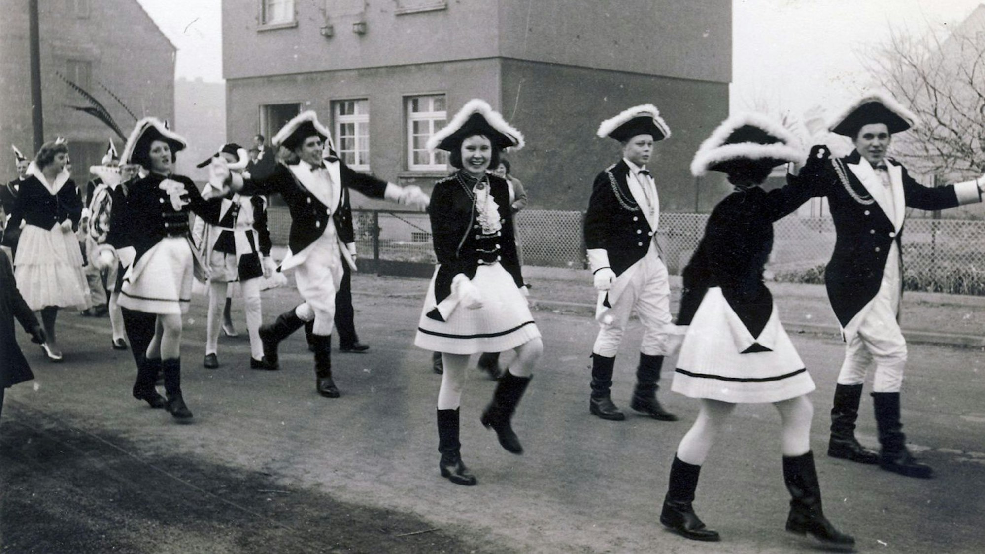 Ein Schwarz-Weiß-Foto zeigt eine Fußgruppe männlicher und weiblicher Karnevalisten.