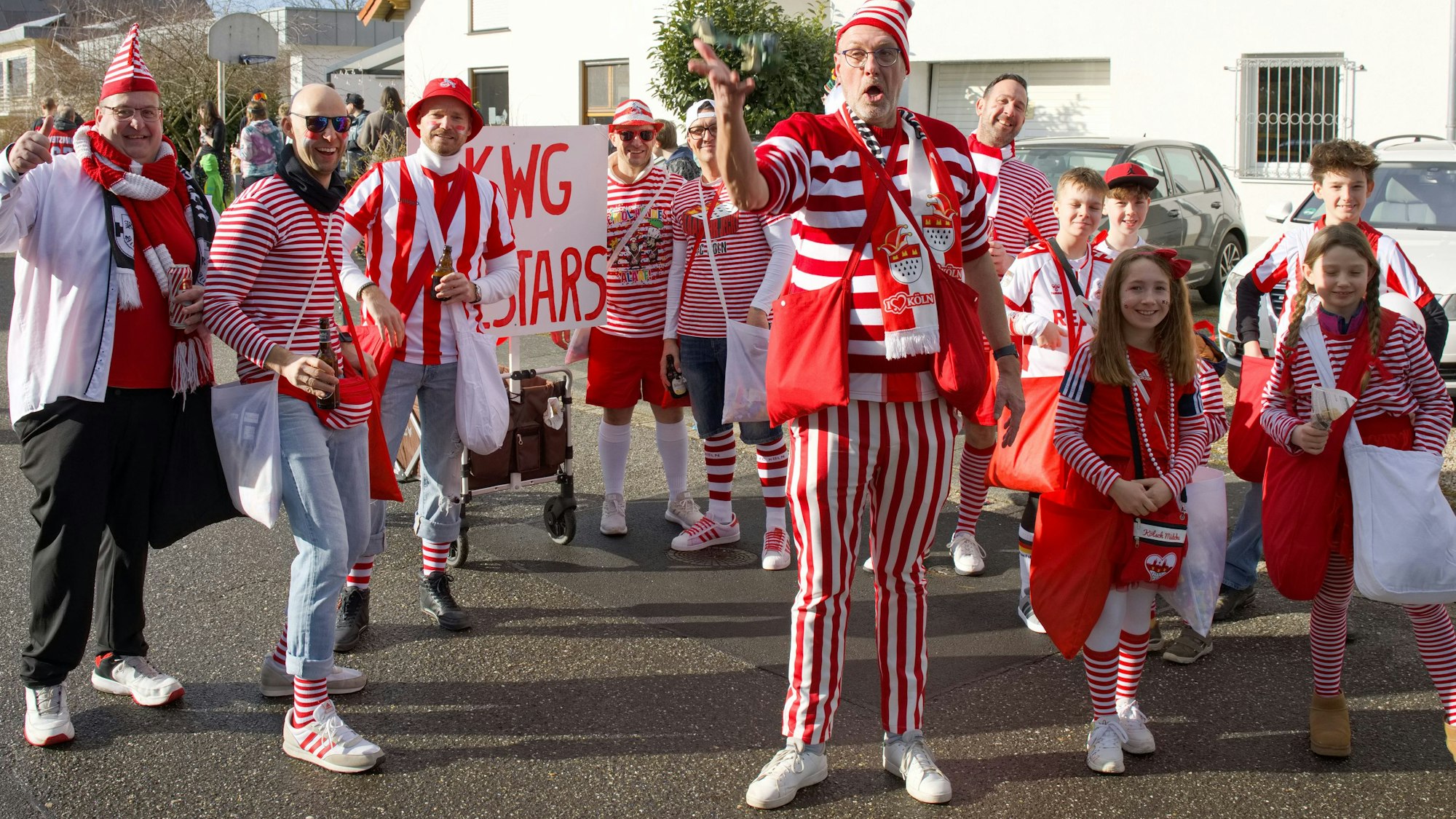 Eine Gruppe rot-weiß kostümierter Kinder und Erwachsener steht auf der Straße in einem Wohnviertel.