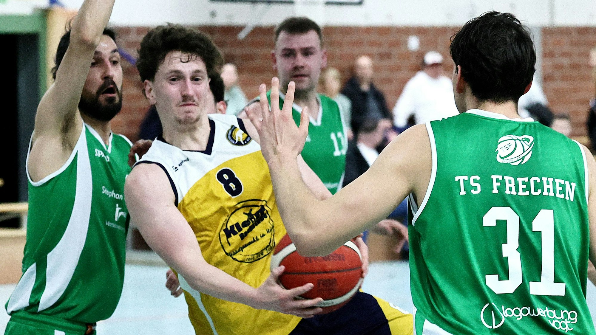 Das Bild zeigt einen Hürther Basketballer im gelben Trikot, der von zwei Frechenern in Grün bedrängt wird.