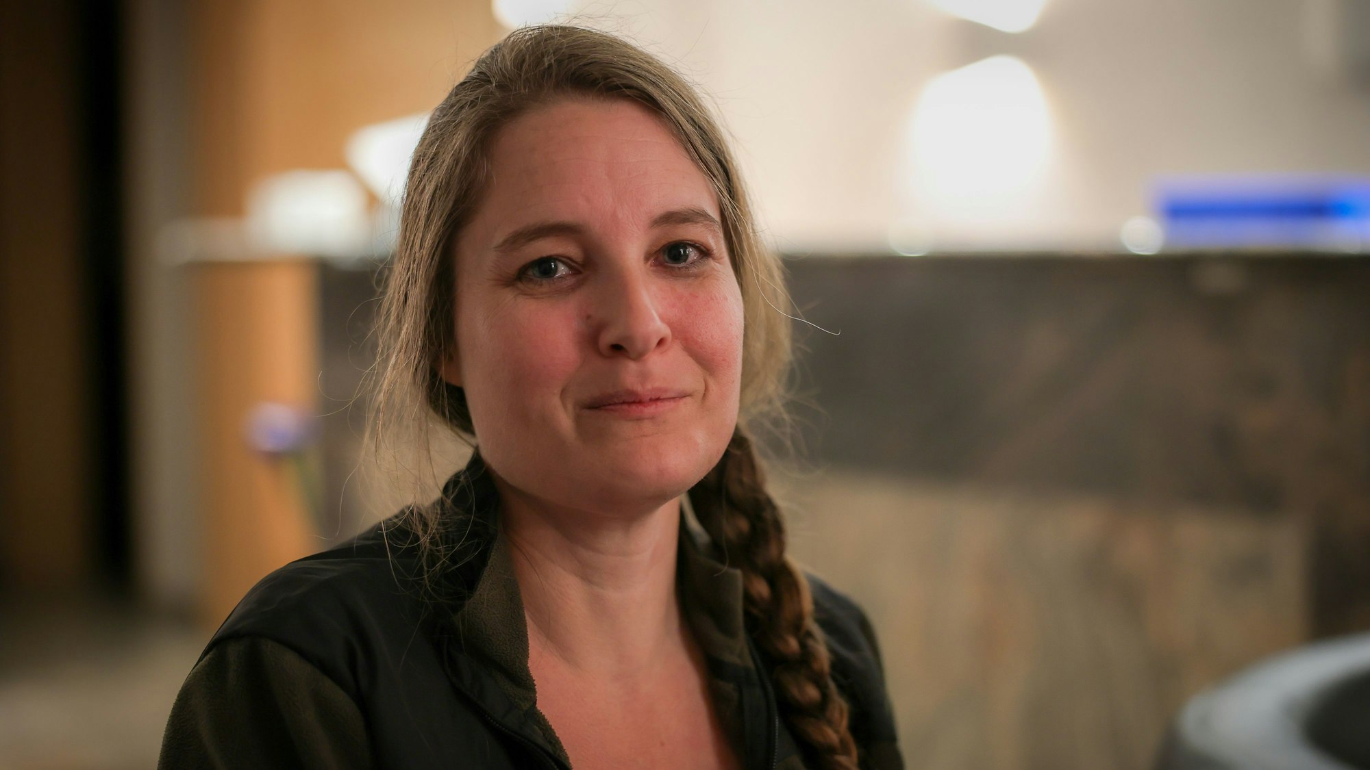 Tina Mommer schaut vor einem unscharf gestellten Hintergrund in die Kamera.