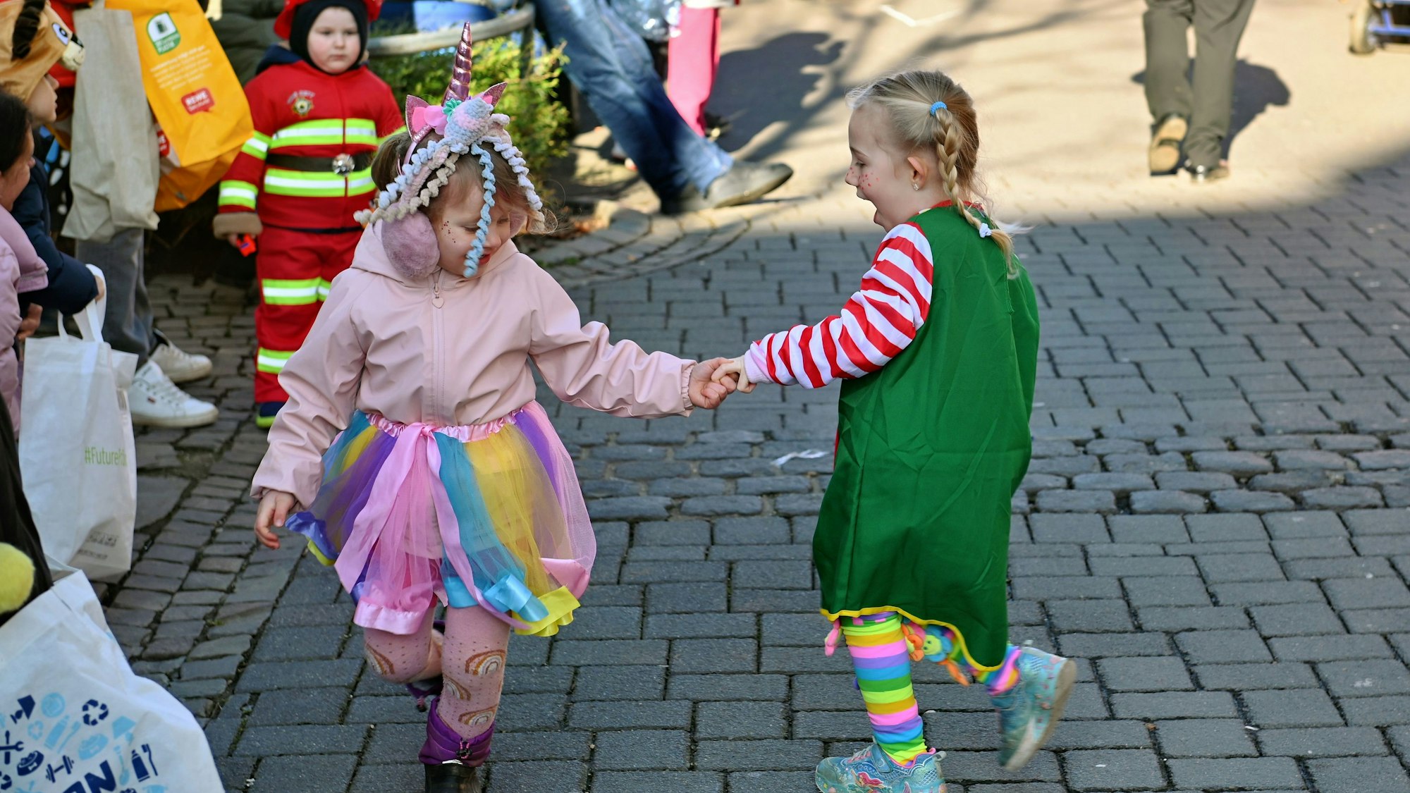 Zwei Mädchen haben sich an einer Hand gefasst und tanzen im Kreis auf der gepflasterten Straße.