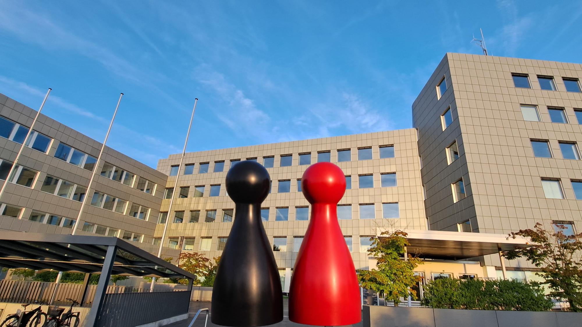 Eine schwarze und eine rote Spielfigur stehen vor dem Kreishaus des Rheinisch-Bergischen Kreises in Bergisch Gladbach-Heidkamp.