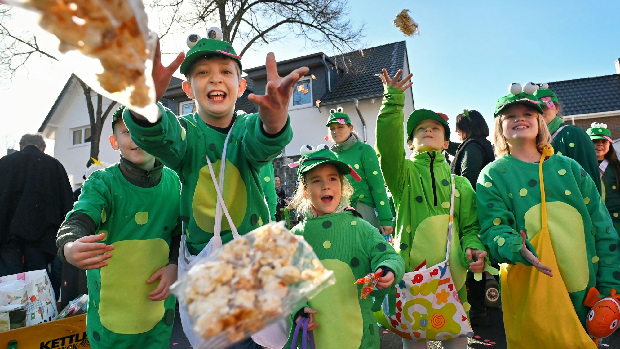 Kinder, die als Frösche verkleidet sind, werfen Kamella auf einem Karnevalszug.