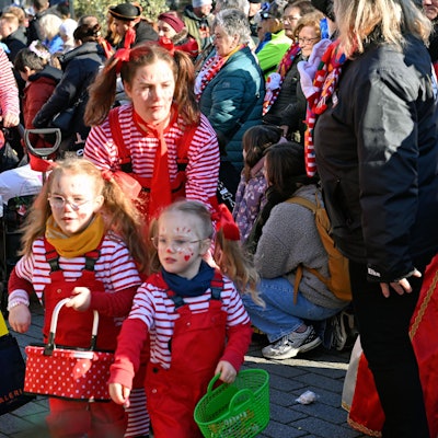 Eine Familie in gestreiften Karnevalskostümen bahnt sich ihren Weg durch die Zuschauer des Kinderzugs in Euskirchen.