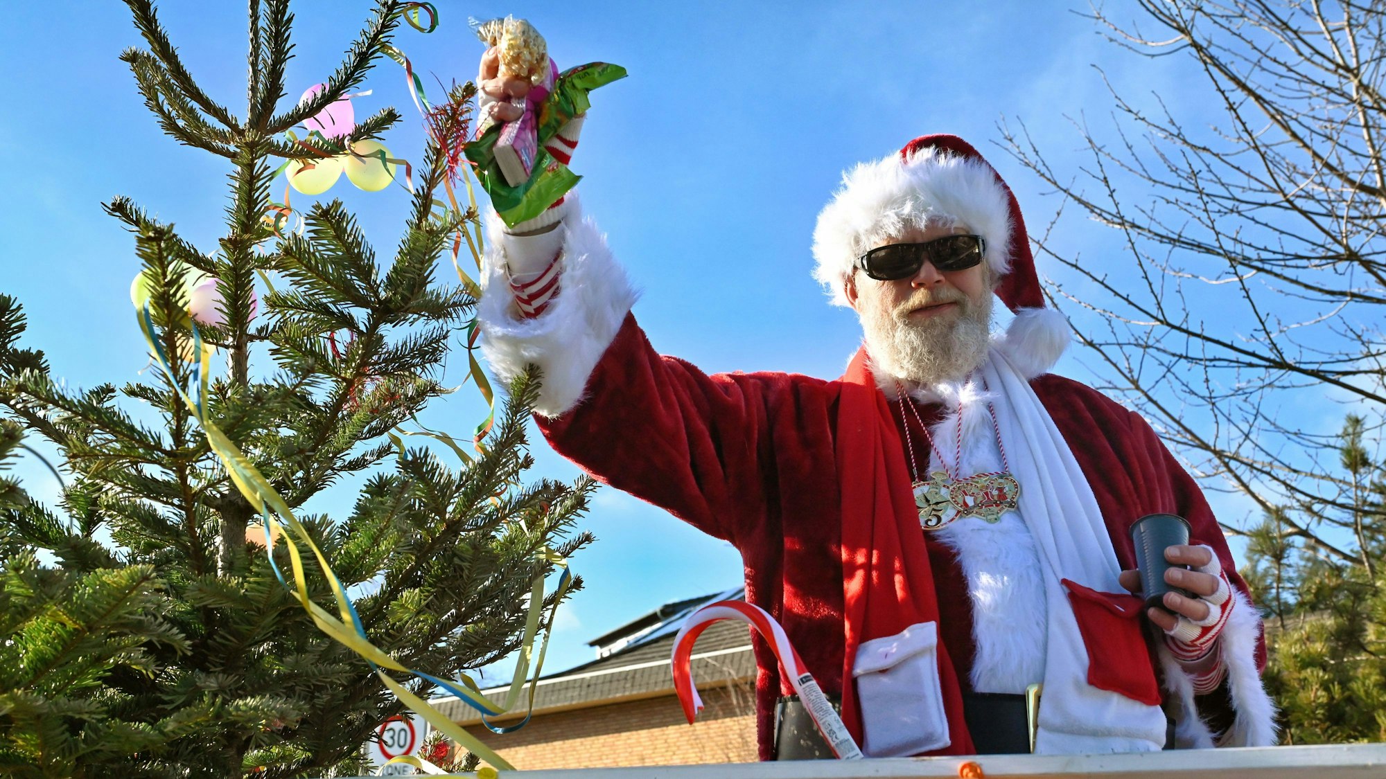 Das Bild zeigt einen Mann, der als Weihnachtsmann verkleidet ist und in einer Hand zahlreiche Kamelle hält.