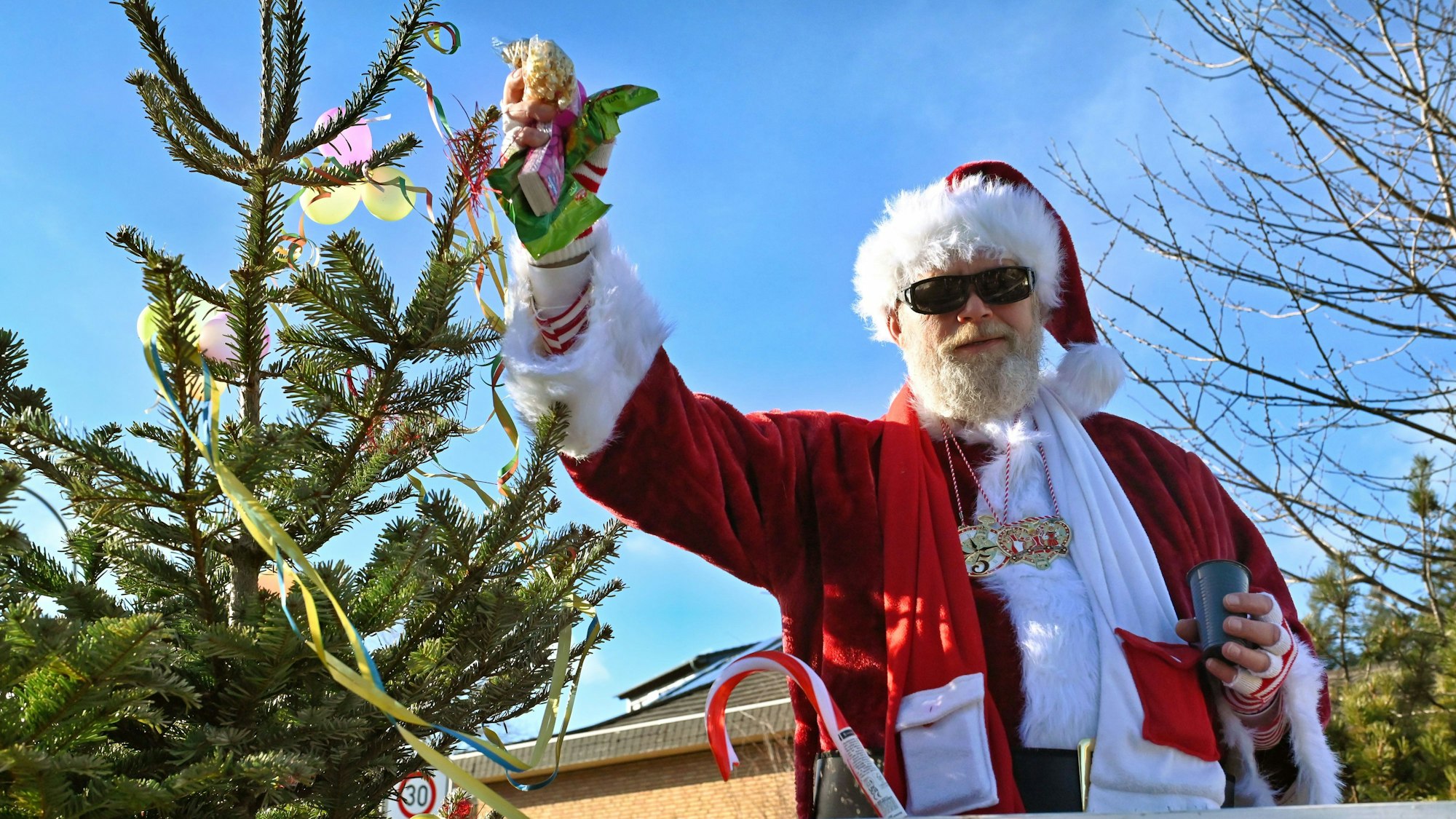 Das Bild zeigt einen Mann, der als Weihnachtsmann verkleidet ist und in einer Hand zahlreiche Kamelle hält.