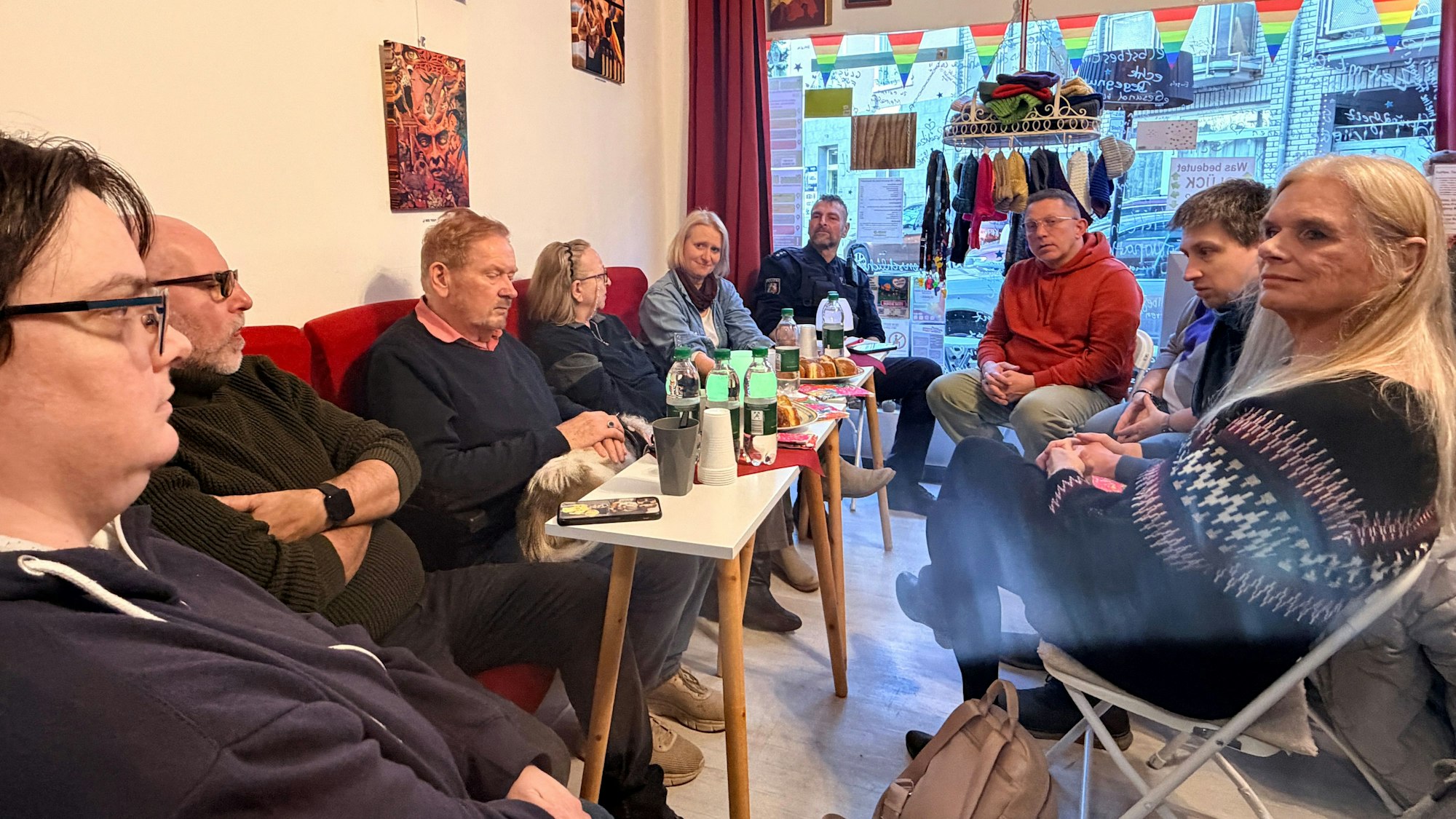 In den Räumen von Simons Glück sitzen die Teilnehmenden. Vor sich auf den Tischen stehen Getränke.