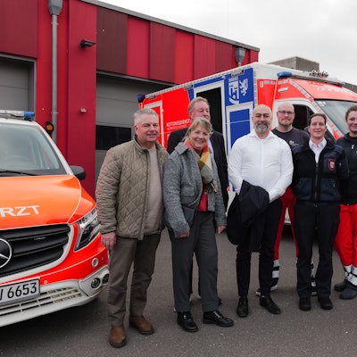 Das Foto zeigt einen Personengruppe und zwei Rettungsfahrzeuge und die Rettungswache im Hintergrund.
