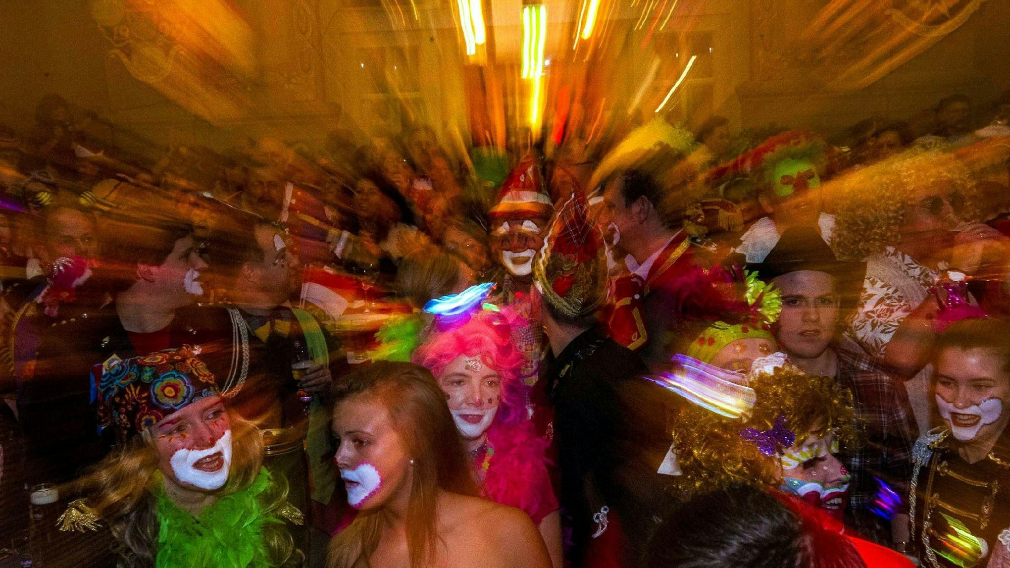 Eine Menge karnevalstisch verkleideter Personen feiert in einem Saal.