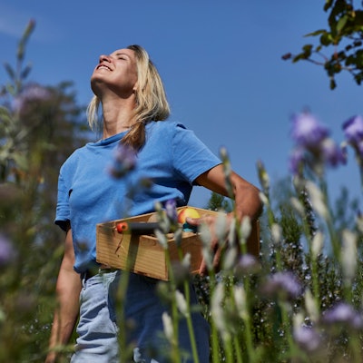 Smiling woman holding a crate in allotment garden