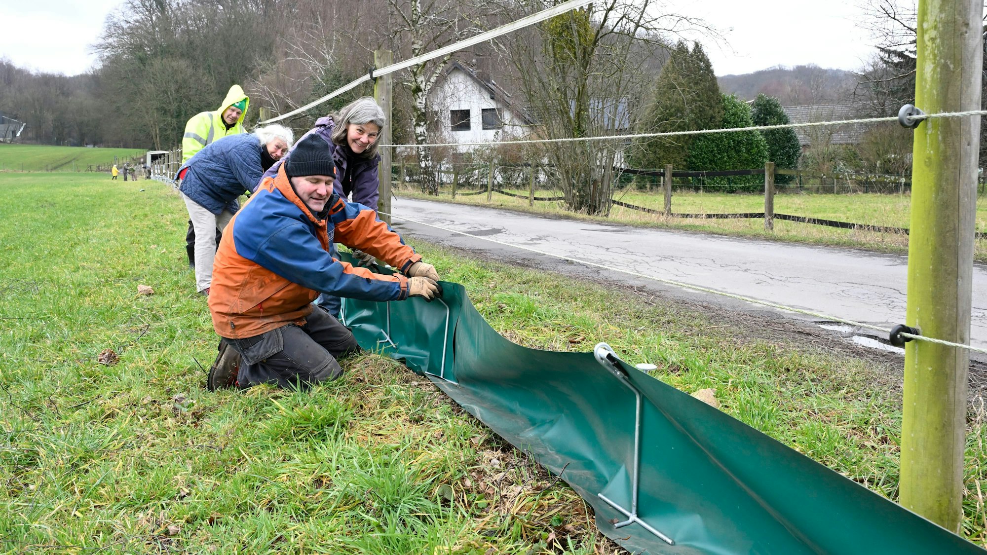 Vier Menschen stecken auf einer Wiese einen grünen Folienzaun in Metallbügel.