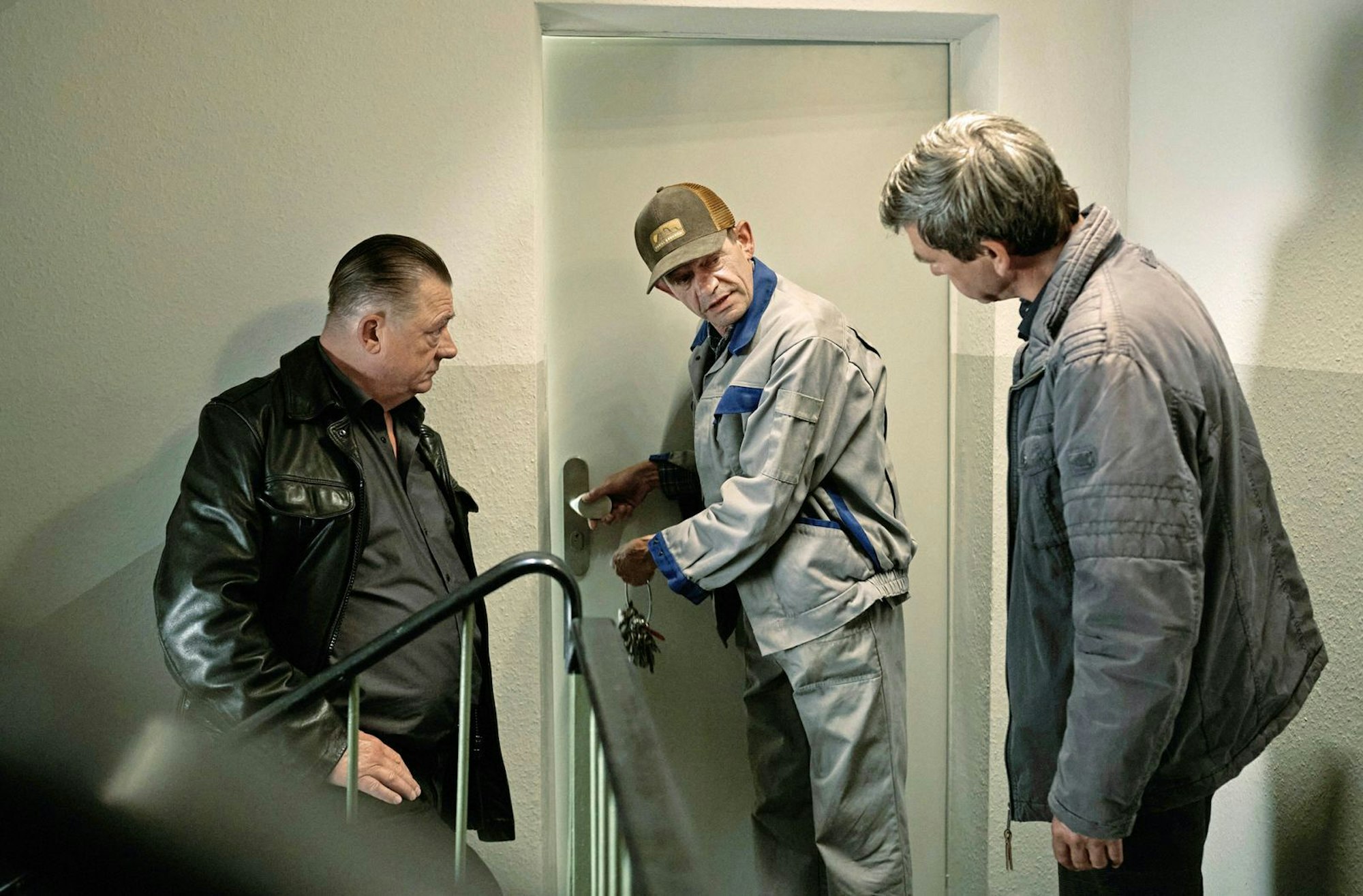 Eine alte Dame, die zurückgezogen lebte, ist tot. Hausmeister Trojanowitz (Henning Peker) öffnet Henry Koitzsch (Peter Kurth, links) und Michael Lehmann (Peter Schneider, rechts) ihre Tür. (Bild: MDR/Felix Abraham)