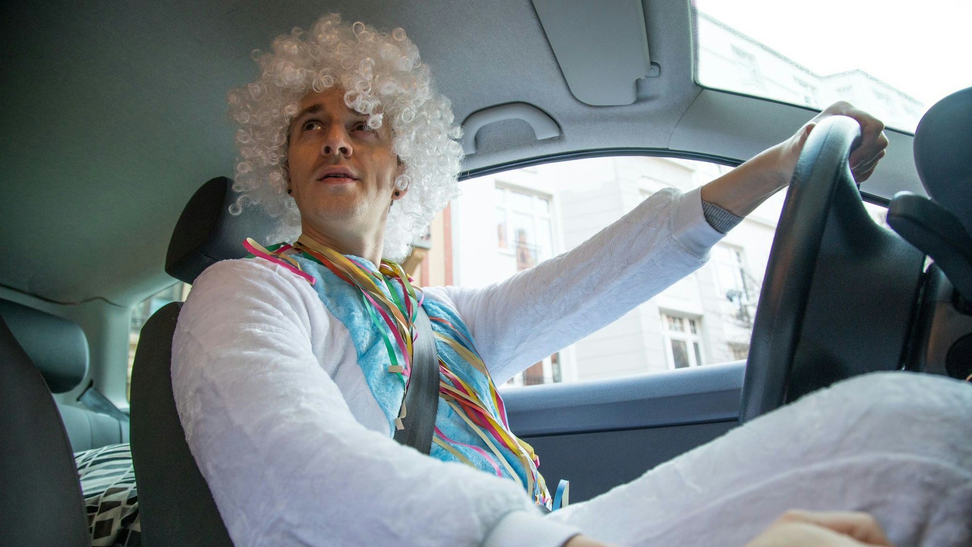 Ein Mann im Kostüm mit Perücke sitzt im Auto.