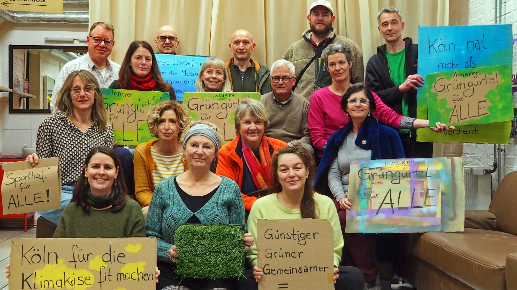 Viele Menschen stehen und hocken mit Protestplakaten in vier Reihen hintereinander.