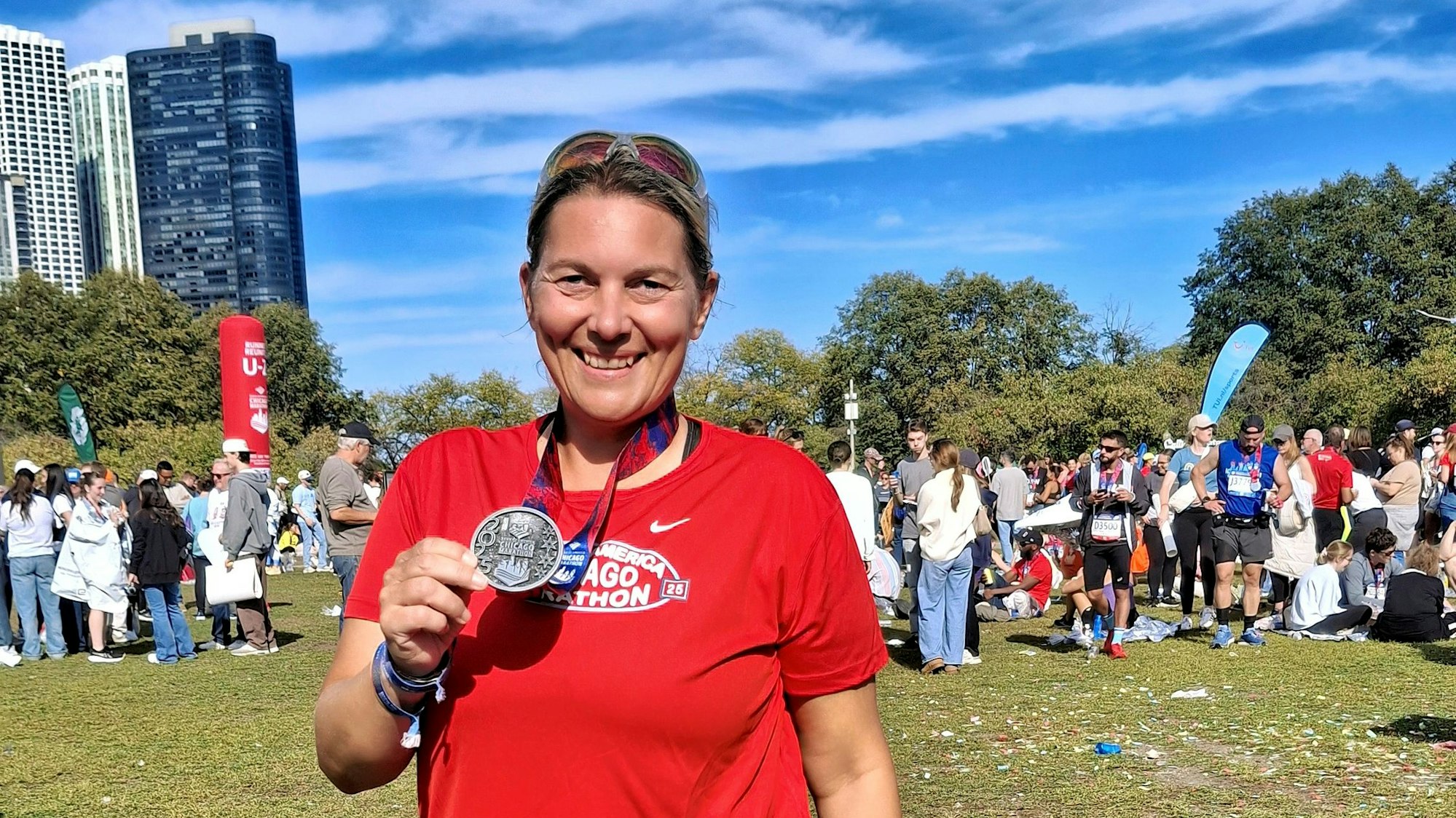 Die Läuferin steht lächelnd in einem Park, hinter ihr weitere Athleten, Zuschauerinnen und Zuschauer und Wolkenkratzer.