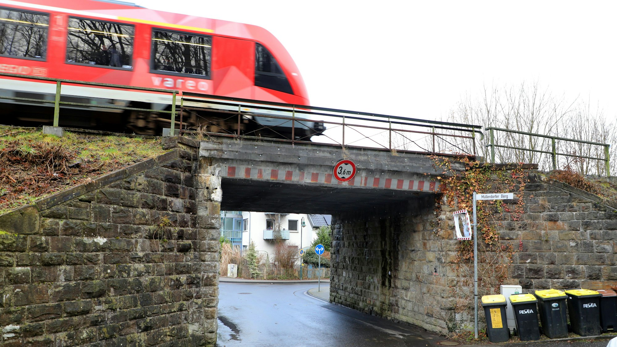 Eine rote Regionalbahn fährt über eine Brücke mit einem schmalen Durchgang.