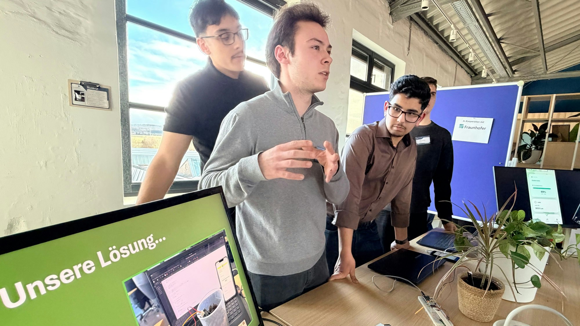 Vier junge Männer erklären an ihrem Stand anhand einer Topfpflanze und entsprechender Hardware das System zur automatischen Pflanzenüberwachung.