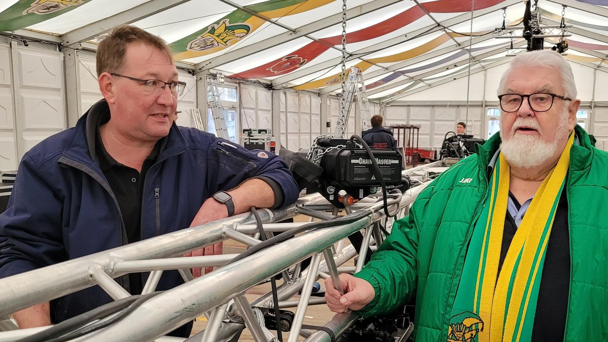 Zwei Männer stehen in einem Festzelt, in dem die Vorbereitungen für die Karnevalstag im Gange sind.