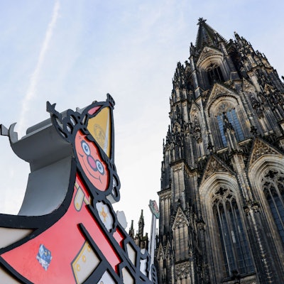 Eine Karnevalsfigur steht vor dem Dom.