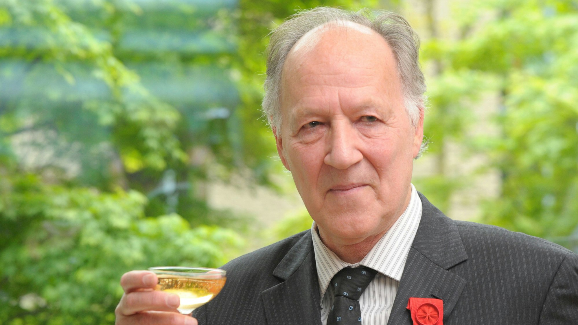 Ein älterer Mann hebt ein Glas und lächelt in die Kamera.