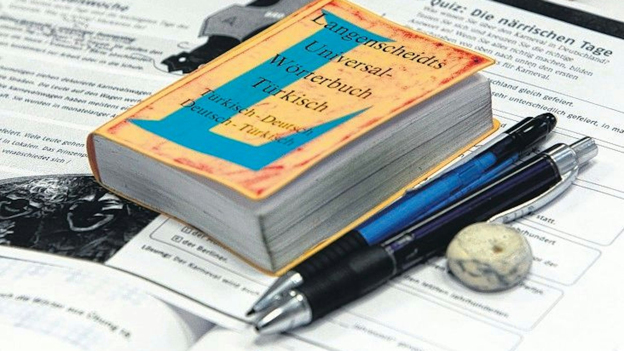 Ein gelbes Wörterbuch Türkisch-Deutsch liegt auf einem Fachbuch. Dazu Kugelschreiber und Radiergummi