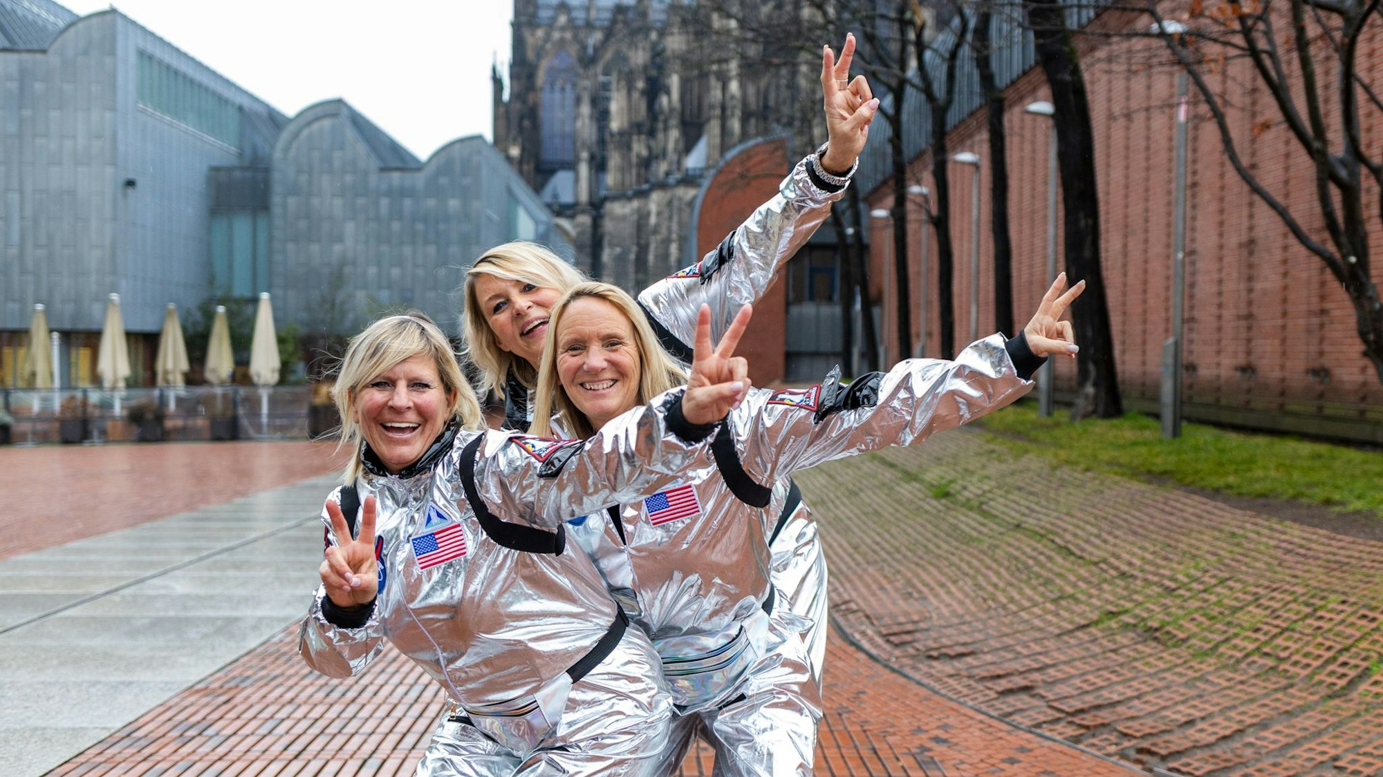 Drei Frauen stehen hintereinander in silbernen Kostümen.