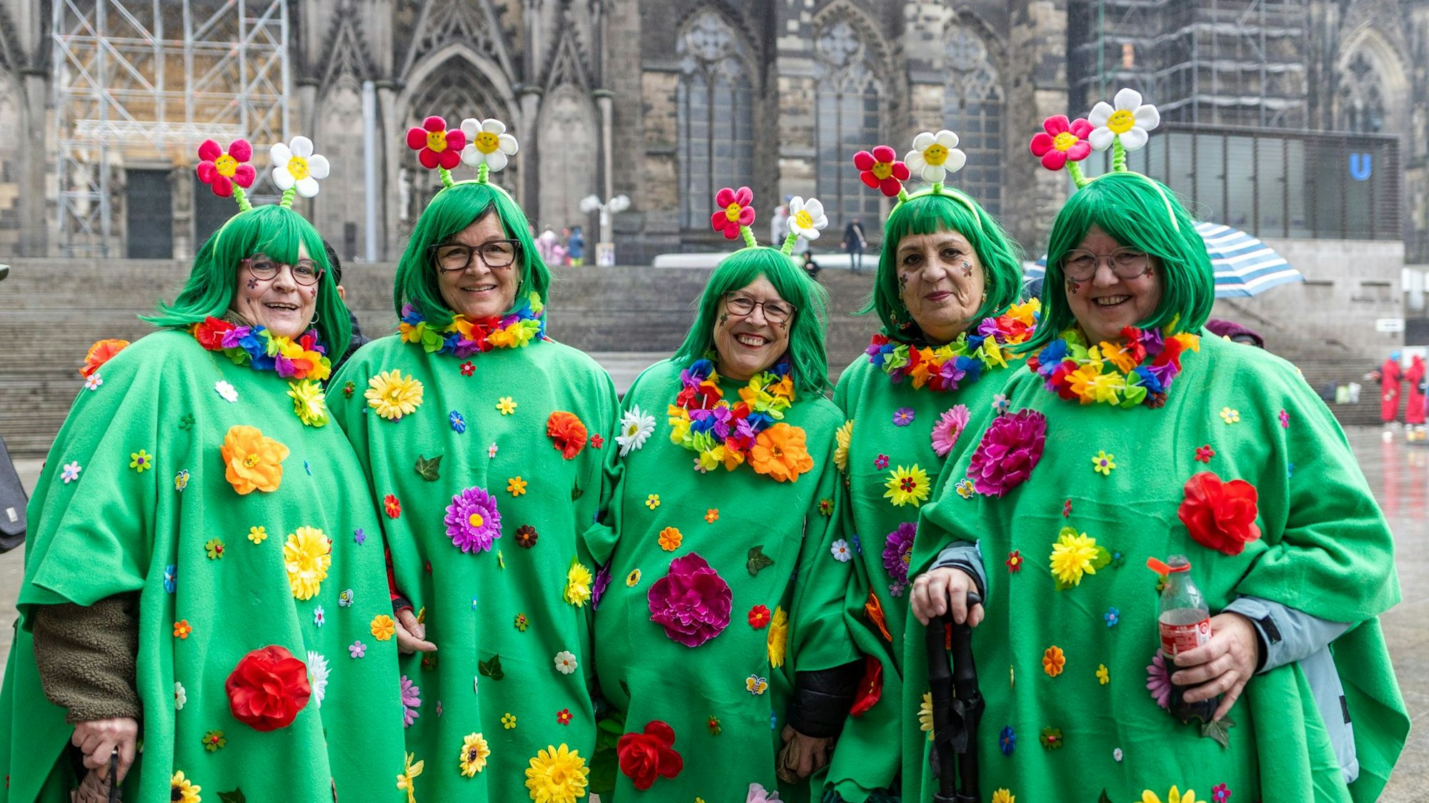 Fünf Frauen tragen grüne Ponchos mit bunten Blumen darauf.
