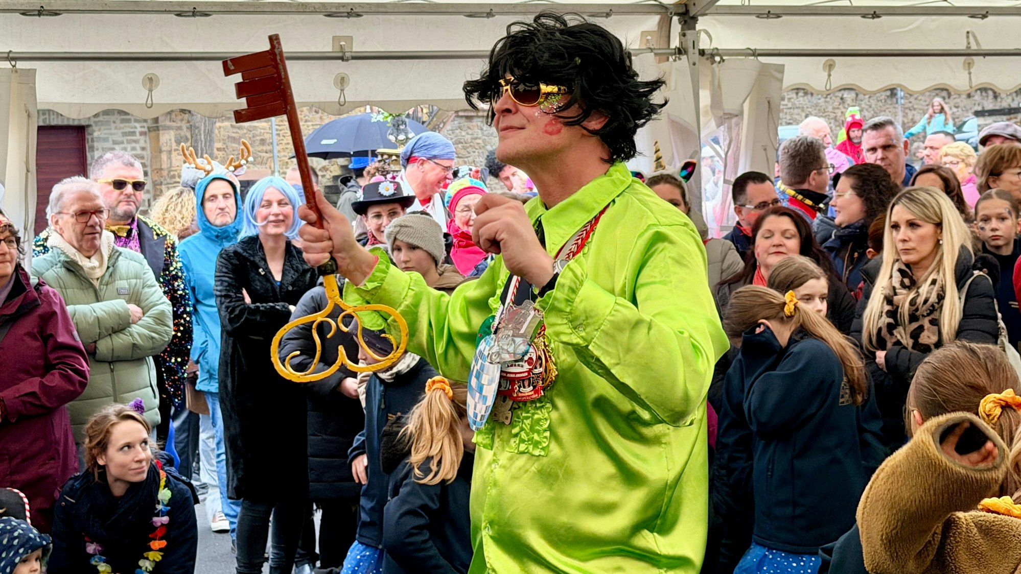 Bürgermeister Sebastian Glatzel im grellgrünen Hemd und mit schwarzer Perücke dirigiert mit dem Stadtschlüssel in der Hand.